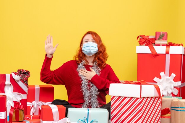 Vista frontale della giovane donna seduta intorno a regali di Natale in maschera sulla parete gialla