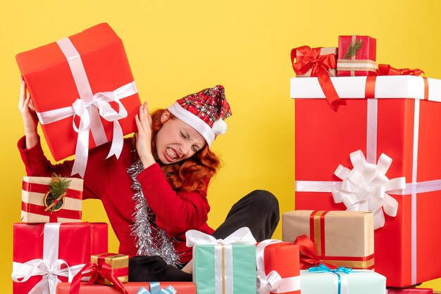 Vista frontale della giovane donna seduta intorno ai regali di Natale sulla parete gialla