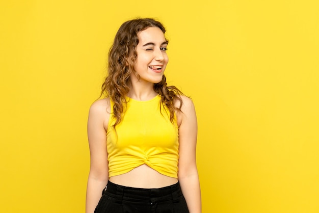 Vista frontale della giovane donna sorridente e ammiccante sulla parete gialla