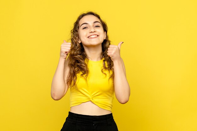 Vista frontale della giovane donna sorridente felicemente sulla parete gialla