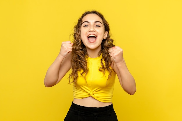 Vista frontale della giovane donna sorridente felicemente sulla parete gialla