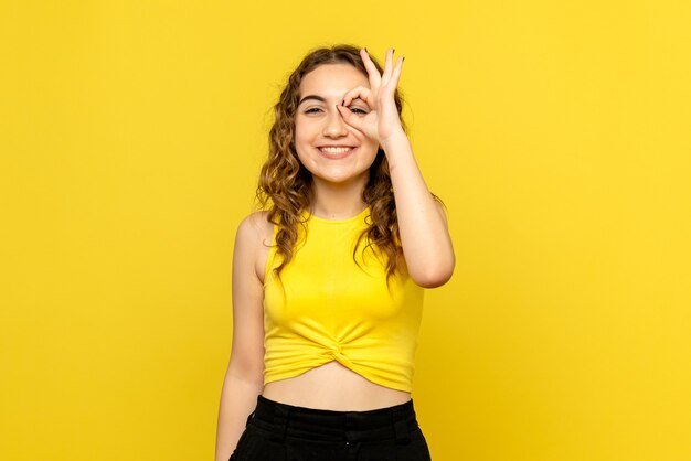 Vista frontale della giovane donna sorridente su una parete gialla
