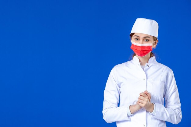 Vista frontale della giovane infermiera sollecitata in tuta medica con maschera rossa sull'azzurro