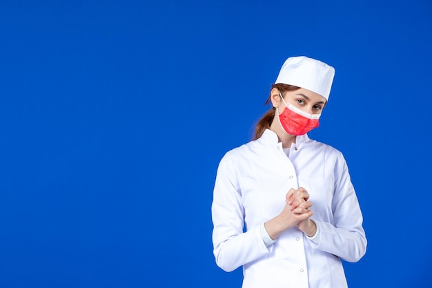 Vista frontale della giovane infermiera sollecitata in tuta medica con maschera rossa sull'azzurro