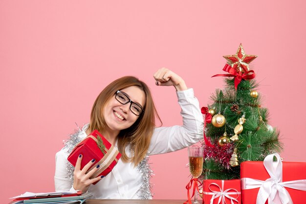 Vista frontale della lavoratrice che si siede con i regali di Natale sul rosa