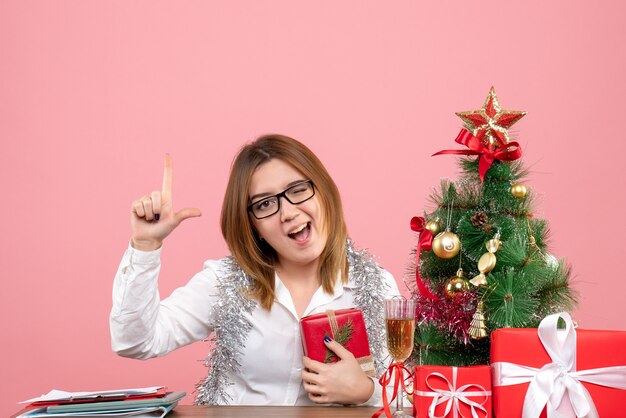 Vista frontale della lavoratrice che si siede con i regali di Natale sul rosa