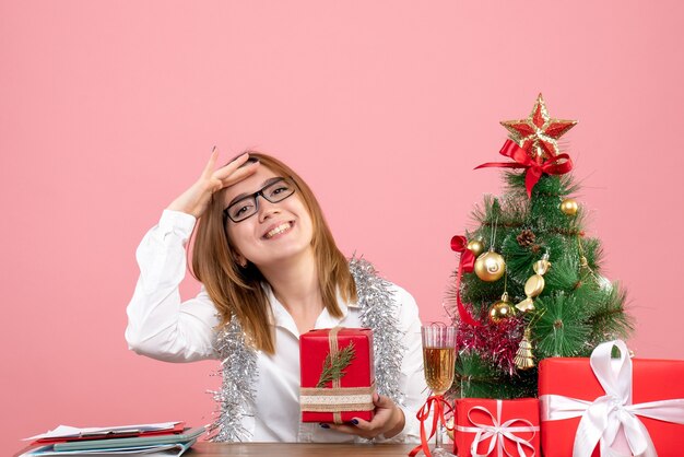 Vista frontale della lavoratrice che si siede con i regali di Natale sul rosa