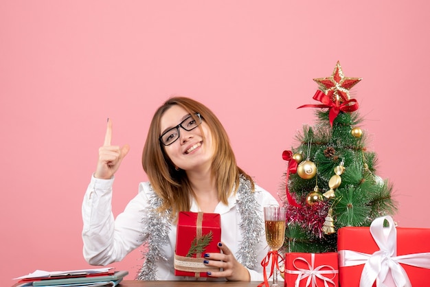 Vista frontale della lavoratrice che si siede con i regali di Natale sul rosa