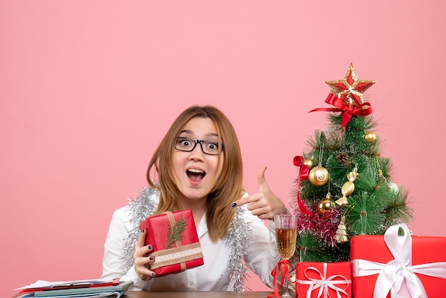 Vista frontale della lavoratrice che si siede con i regali di Natale sul rosa