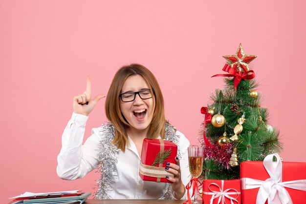 Vista frontale della lavoratrice che si siede con i regali di Natale sul rosa