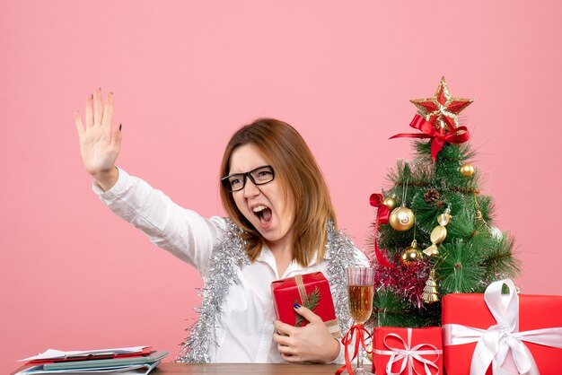 Vista frontale della lavoratrice che si siede con i regali di Natale sul rosa