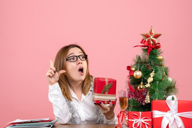 Vista frontale della lavoratrice che si siede con i regali di Natale sul rosa