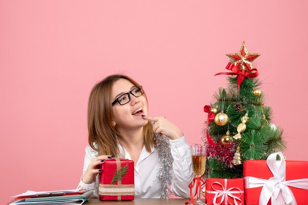 Vista frontale della lavoratrice che si siede con i regali di Natale sul rosa