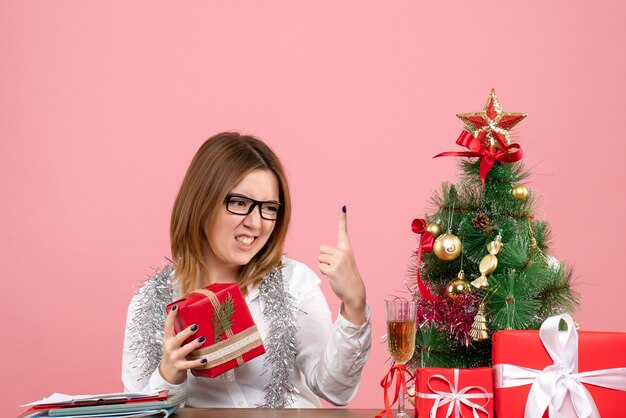 Vista frontale della lavoratrice che si siede con i regali di Natale sul rosa