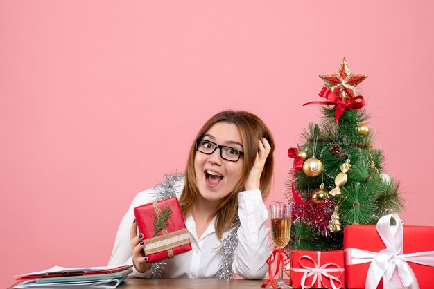 Vista frontale della lavoratrice che si siede intorno ai regali di Natale e all'albero sul rosa