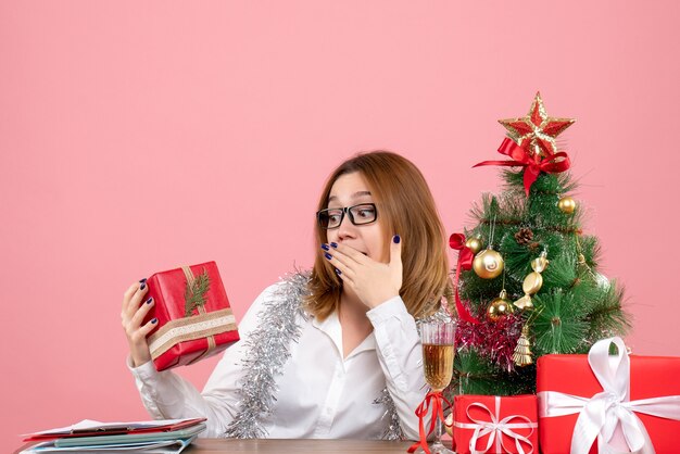 Vista frontale della lavoratrice che si siede intorno ai regali di Natale e all'albero sul rosa