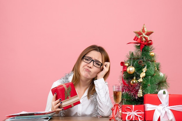 Vista frontale della lavoratrice che si siede intorno ai regali di Natale e all'albero sul rosa