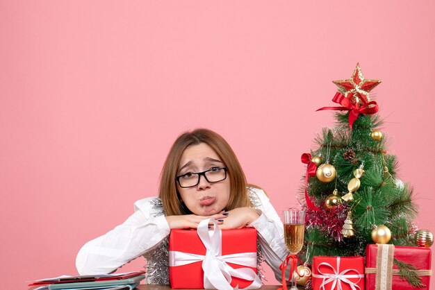 Vista frontale della lavoratrice che si siede intorno ai regali di Natale e all'albero sul rosa