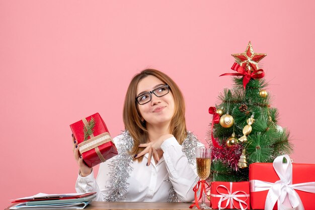 Vista frontale della lavoratrice che si siede intorno ai regali di Natale e all'albero sul rosa