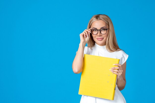 Vista frontale della lavoratrice in abito bianco che tiene cartella gialla e sorride sulla parete blu