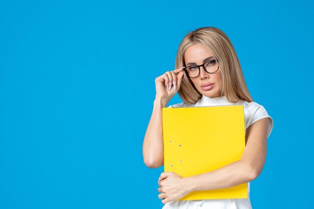 Vista frontale della lavoratrice in abito bianco che tiene cartella gialla sulla parete blu