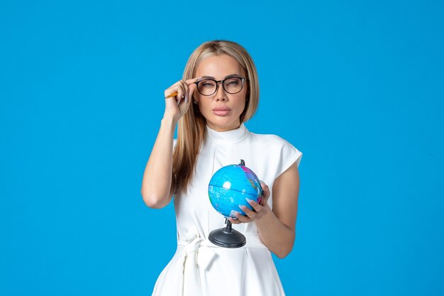 Vista frontale della lavoratrice in abito bianco che tiene un piccolo globo terrestre sulla parete blu