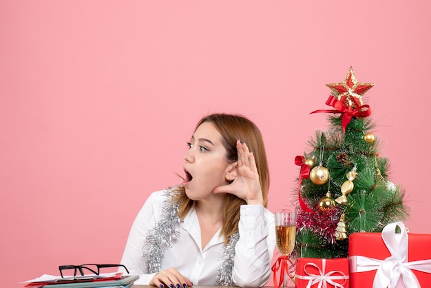 Vista frontale della lavoratrice seduta dietro il suo tavolo con i regali di Natale in ascolto sul rosa