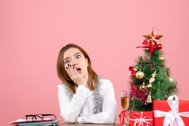 Vista frontale della lavoratrice seduta dietro il suo tavolo con regali di Natale in rosa