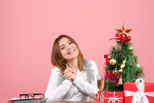 Vista frontale della lavoratrice seduta dietro il suo tavolo con regali di Natale in rosa