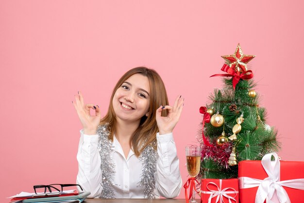 Vista frontale della lavoratrice seduta dietro il suo tavolo con regali in rosa