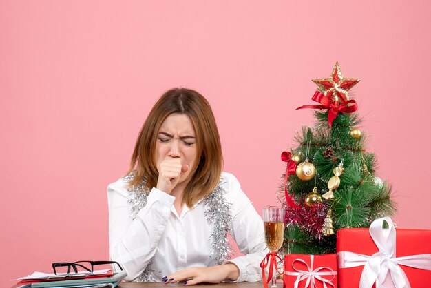 Vista frontale della lavoratrice seduta intorno a regali di Natale tosse sul rosa
