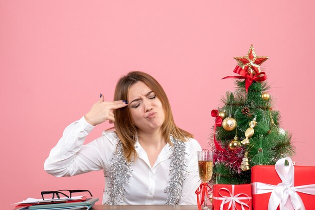 Vista frontale della lavoratrice seduta intorno ai regali di Natale sul rosa