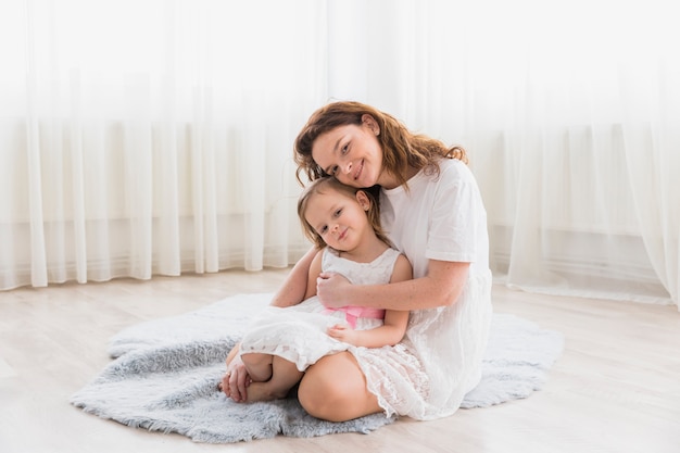 Vista frontale della madre con la sua ragazza del bambino che si siede sul tappeto lanuginoso nella casa