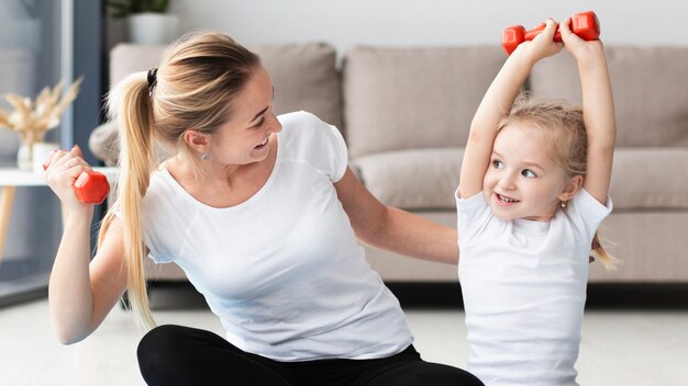 Vista frontale della madre e della figlia che si esercitano con i pesi a casa