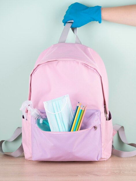 Vista frontale della mano con guanto chirurgico che tiene la borsa del libro con mascherina medica e disinfettante