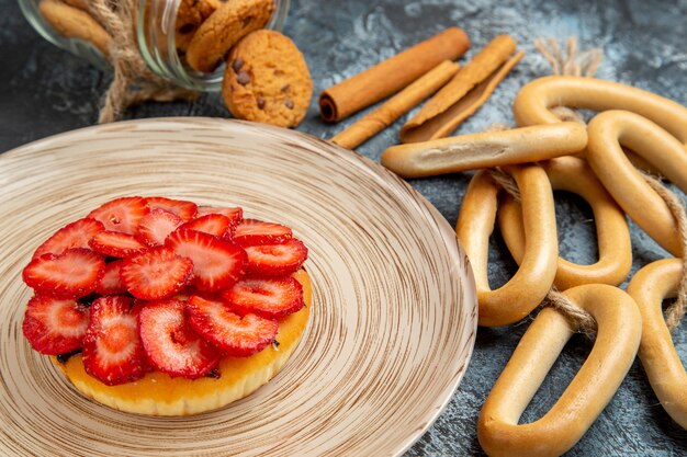 Vista frontale della piccola torta fruttata con cracker sulla superficie scura