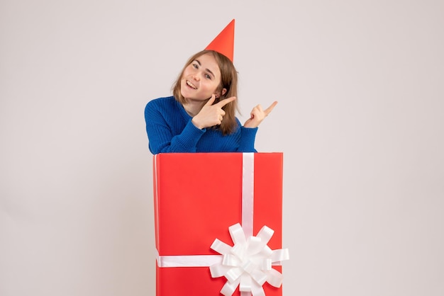 Vista frontale della ragazza all'interno della scatola regalo rossa sul muro bianco