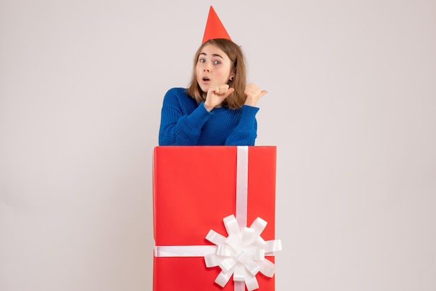 Vista frontale della ragazza all'interno della scatola regalo rossa sul muro bianco