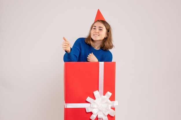 Vista frontale della ragazza all'interno della scatola regalo rossa sul muro bianco