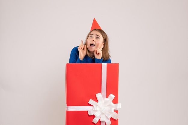 Vista frontale della ragazza all'interno della scatola regalo rossa sul muro bianco