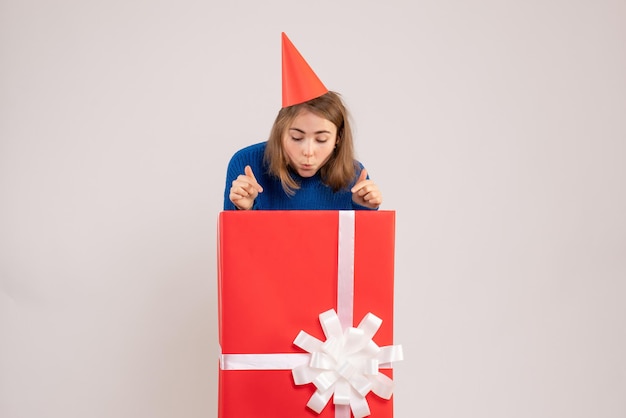 Vista frontale della ragazza all'interno della scatola regalo rossa sul muro bianco