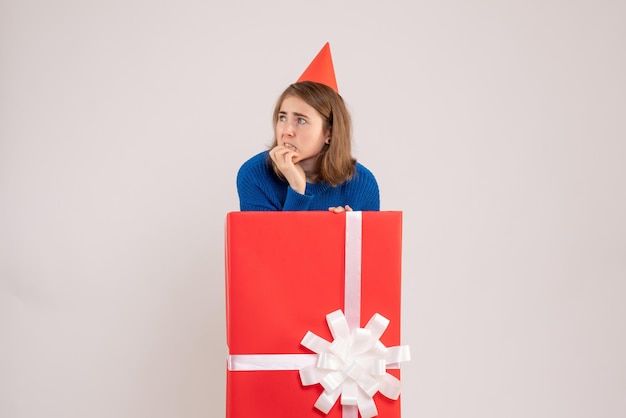 Vista frontale della ragazza all'interno della scatola regalo rossa sul muro bianco