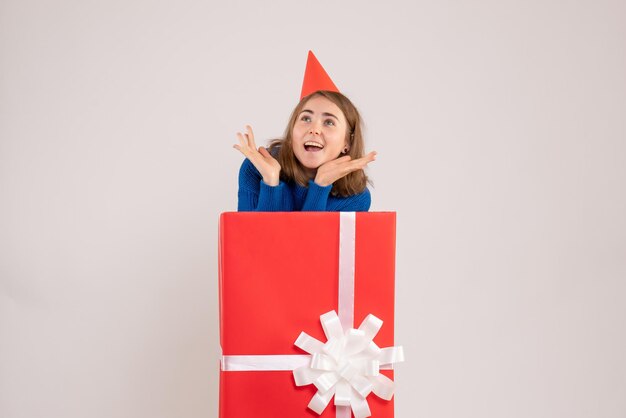 Vista frontale della ragazza all'interno della scatola regalo rossa sul muro bianco