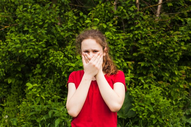 Vista frontale della ragazza che esamina macchina fotografica che copre la sua bocca del parco