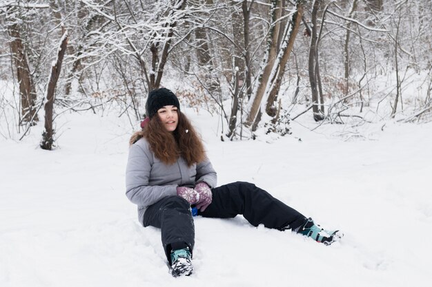 Vista frontale della ragazza che indossa vestiti caldi che si siedono sulla neve