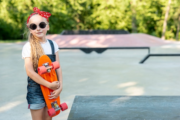 Vista frontale della ragazza con skateboard arancione