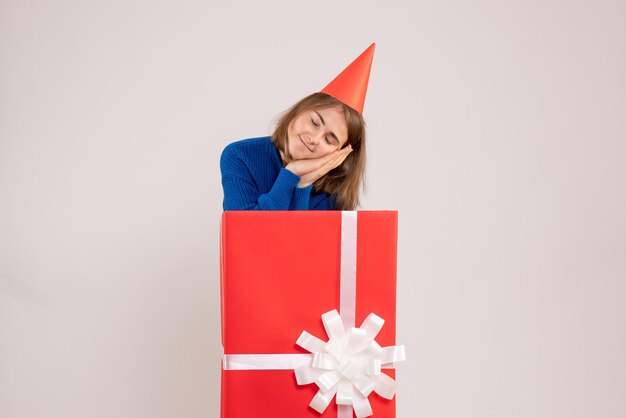 Vista frontale della ragazza dentro la scatola regalo rossa che dorme su un muro bianco