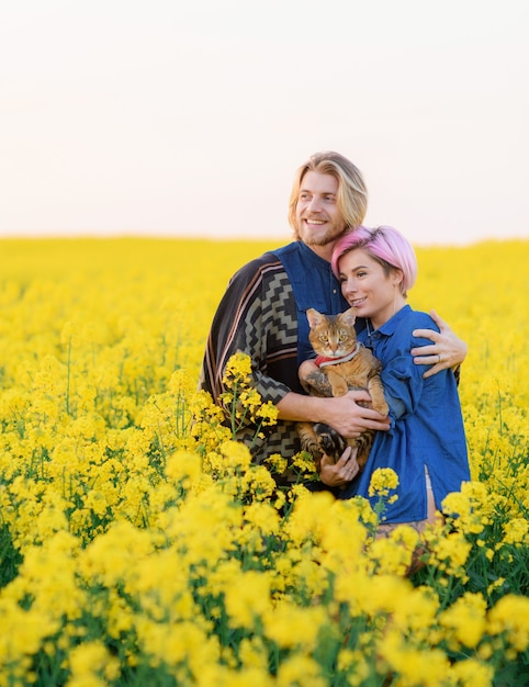 Vista frontale della ragazza sorridente con il suo ragazzo, in piedi tra il campo con il gatto e distogliendo lo sguardo