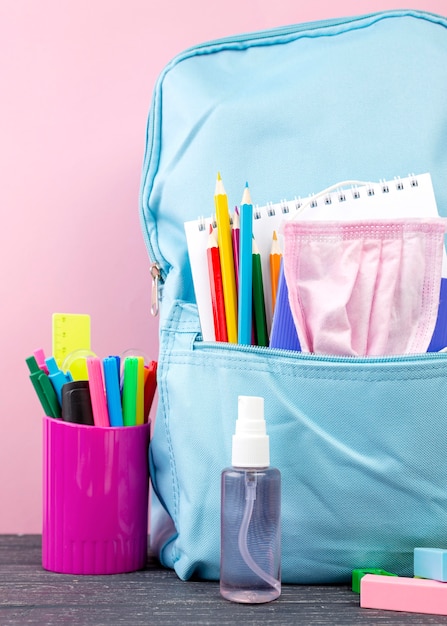 Vista frontale della schiena a cancelleria della scuola con zaino e disinfettante per le mani