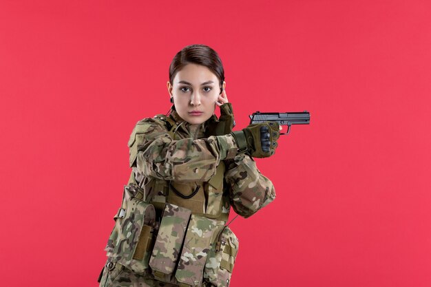 Vista frontale della soldatessa in mimetica che tiene la pistola sul muro rosso